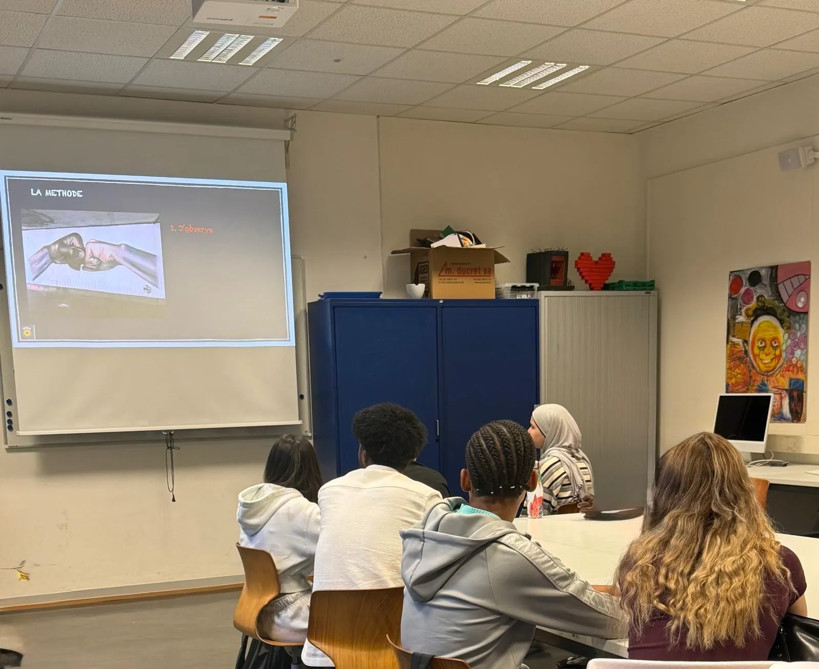 Élèves pendant un atelier WHAT, une diapositive « La méthode : 1. J'observe » projetée au mur